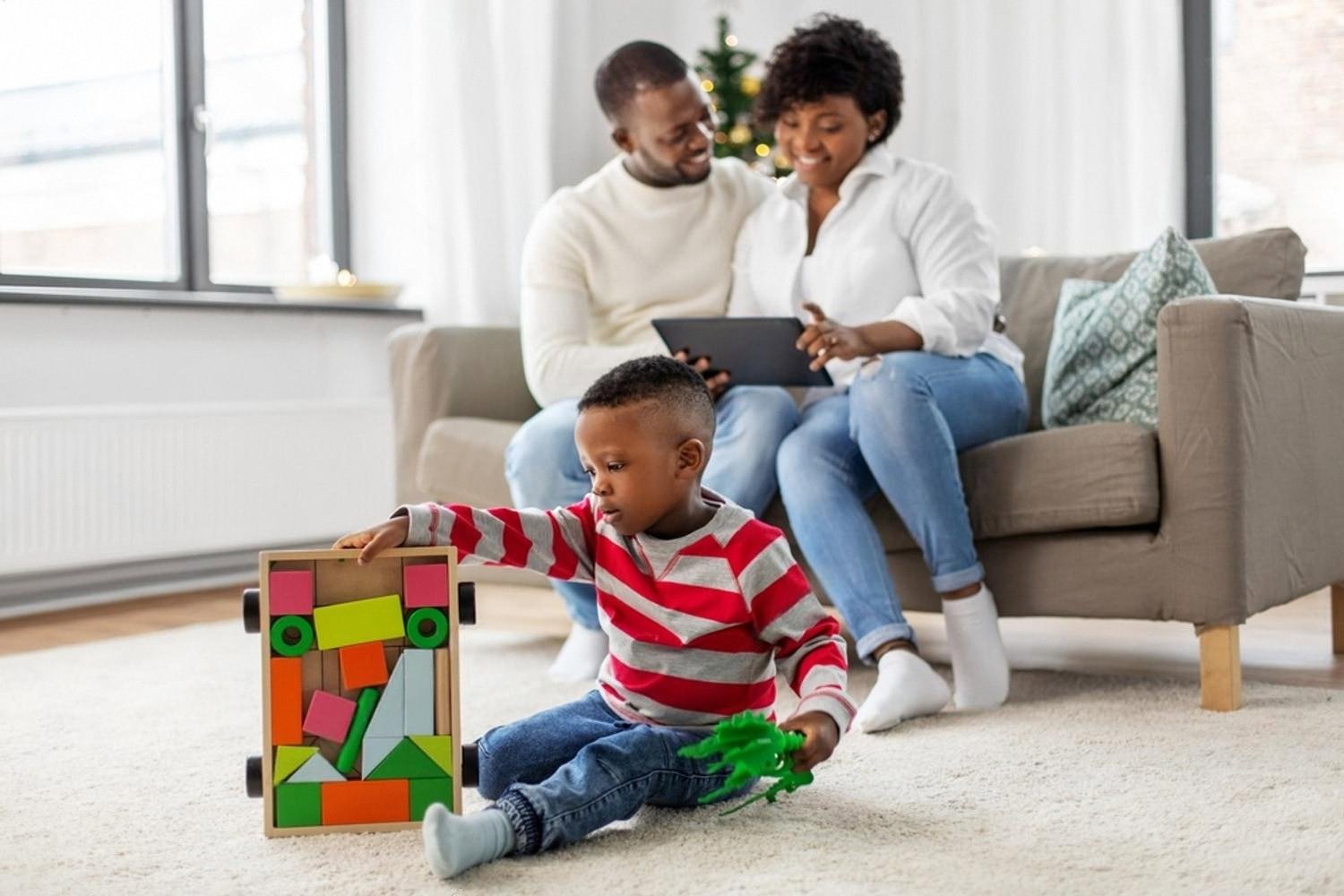 Parents in a living room watching their young son play with a wooden block set