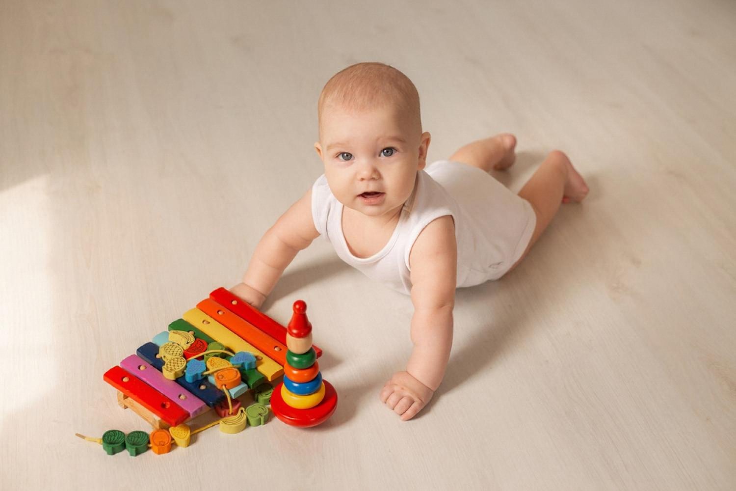 Baby on the floor next to a wooden xylophone and stacking rings