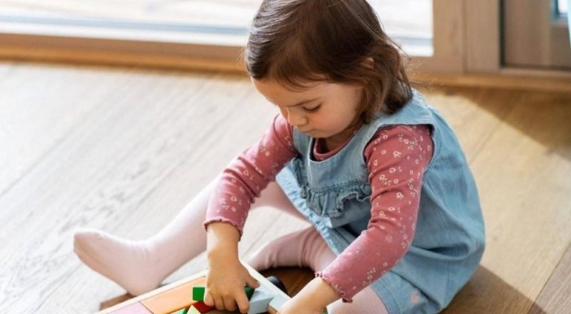 Toddler girl playing with a wooden block wagon on a hardwood floor