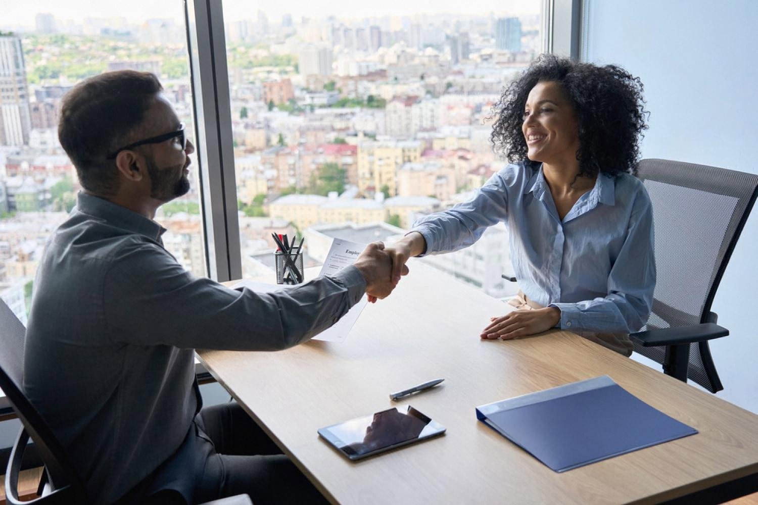 Manager shaking hands with a candidate during a leadership assessment interview in a high-rise office
